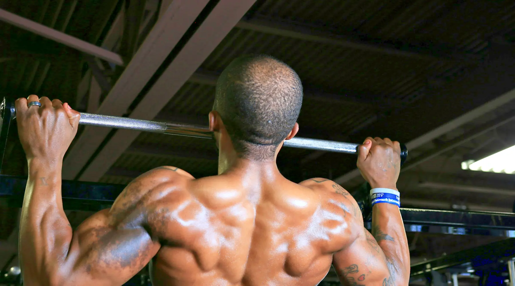 A man pulls himself up on a pull-up bar, seen from behind