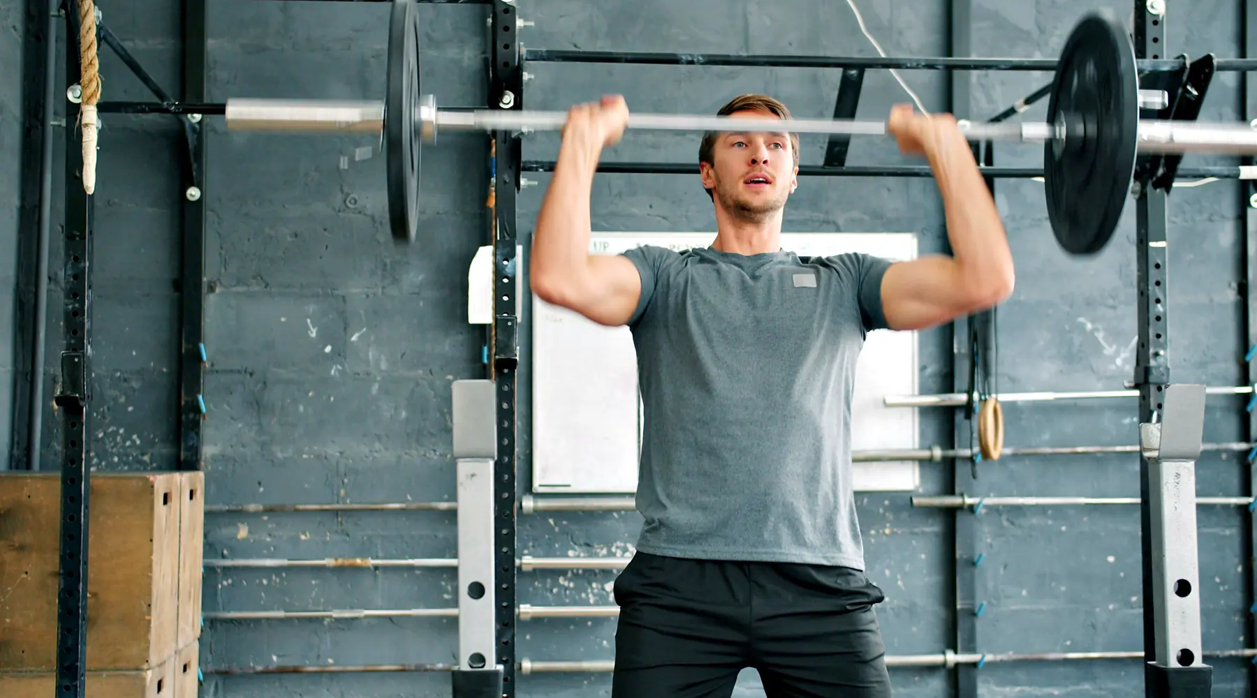 A man presses a barbell overhead in a squat rack
