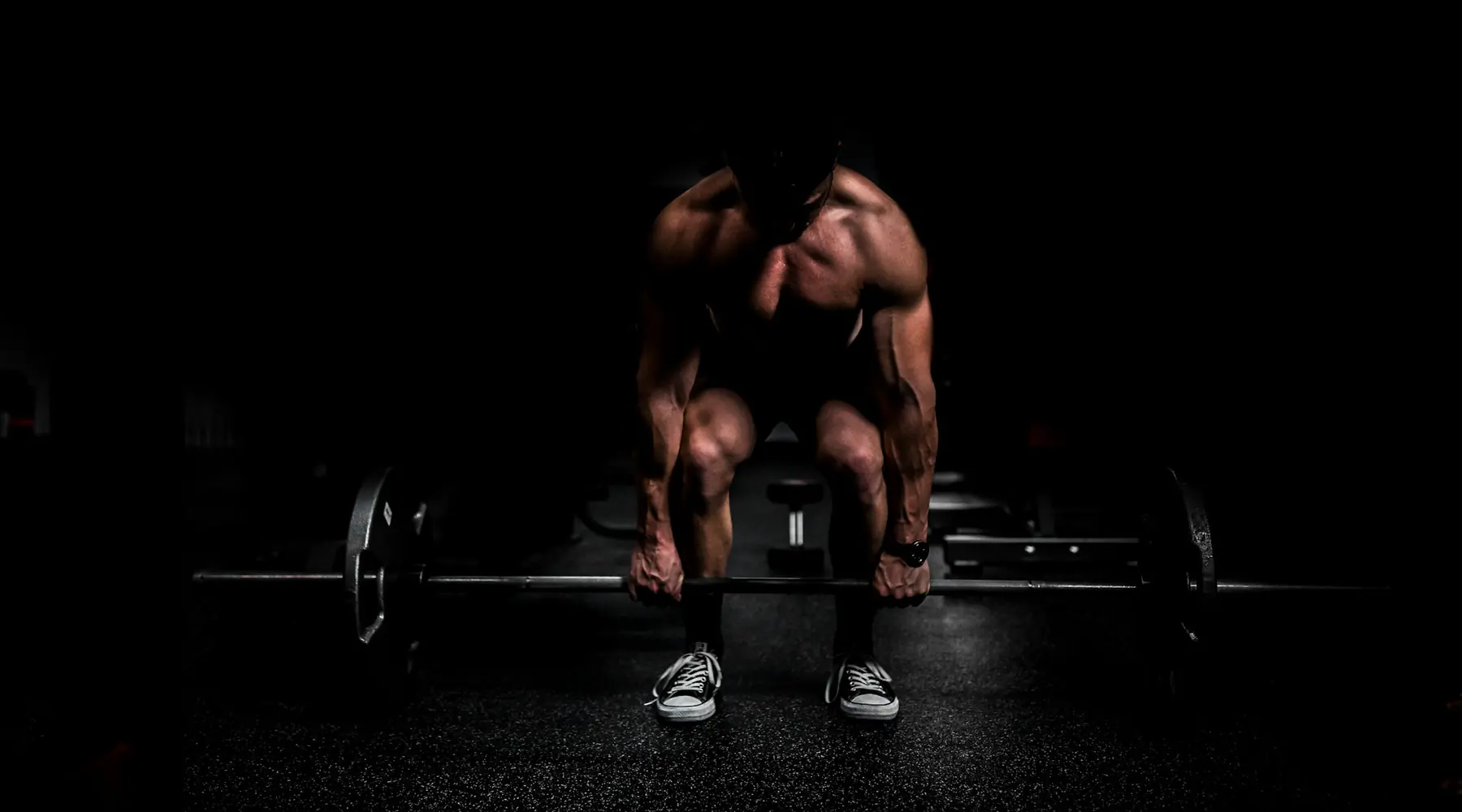 A lifter crouched over a barbell in a dark gym, about to pull