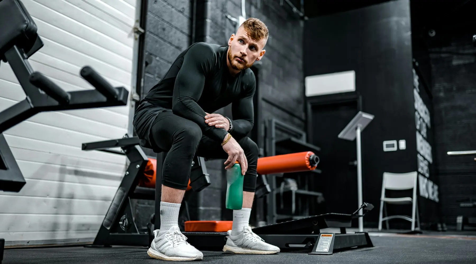 An athlete sitting on a bench with a water bottle, resting between sets