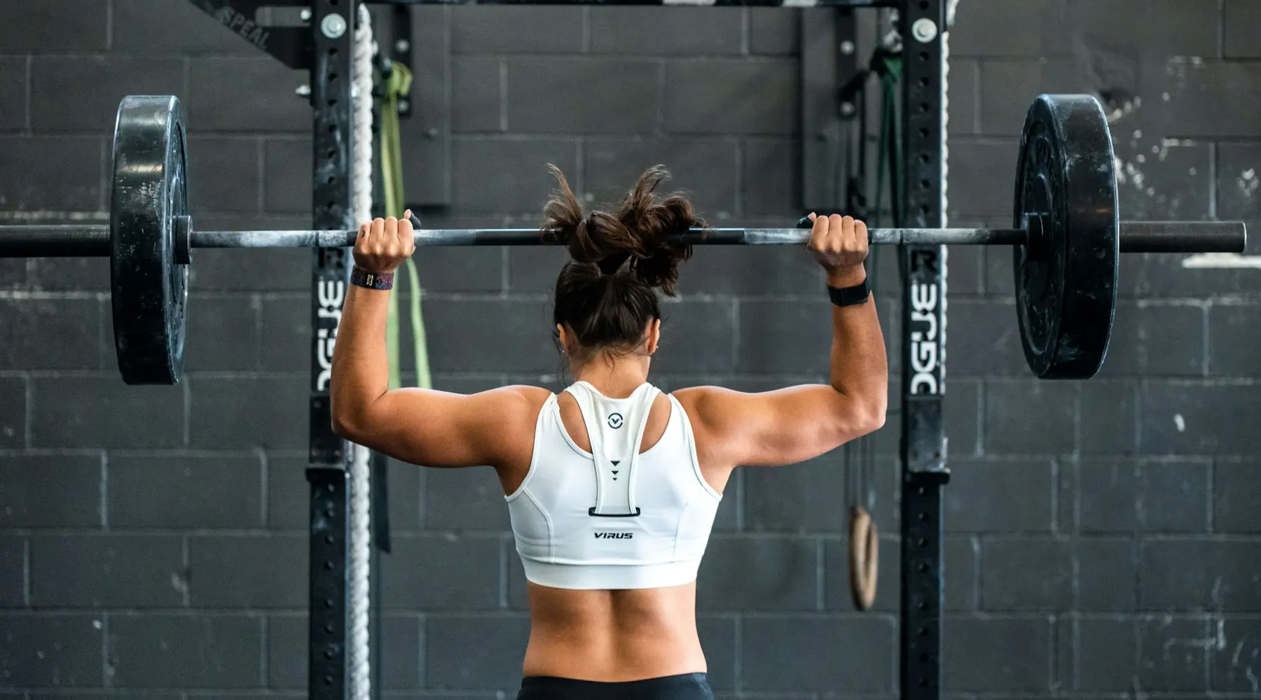 A woman pressing a barbell overhead in a squat rack