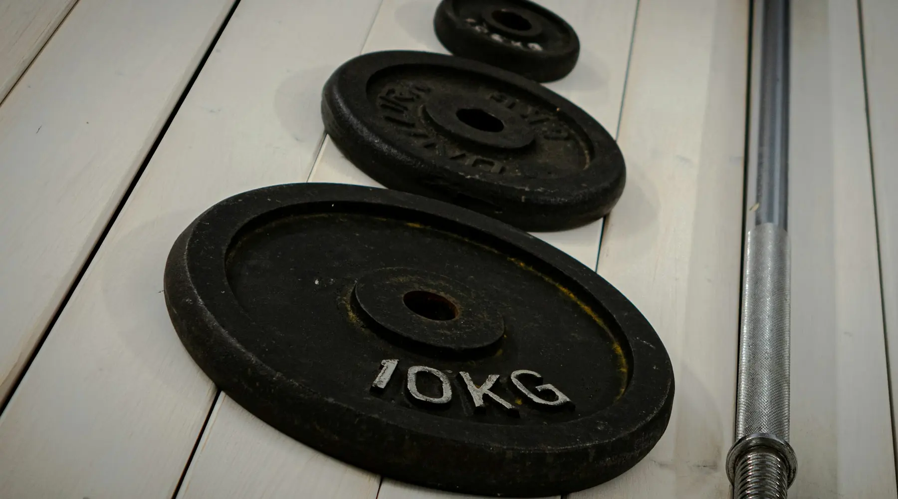 Iron weight plates and a barbell sleeve on a wooden floor